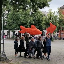 eine Gruppe von Menschen trägt zwei große orangene Fische