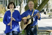 Frau mit Flöte lacht, Mann mit Gitarre schaut ernst