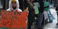 person im hühnerkostüm mit orangem schild wo 'ostern vegan' steht